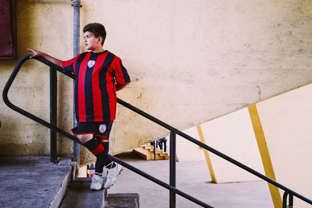 man in red and black stripe polo shirt and black pants standing on black metal bar