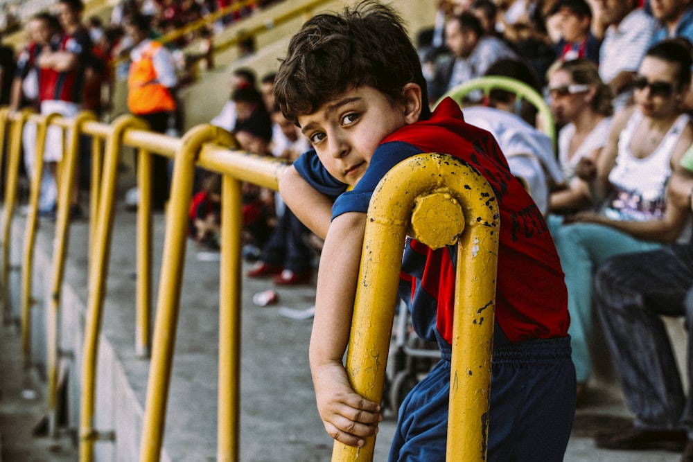 boy in blue and red shirt holding yellow metal bar