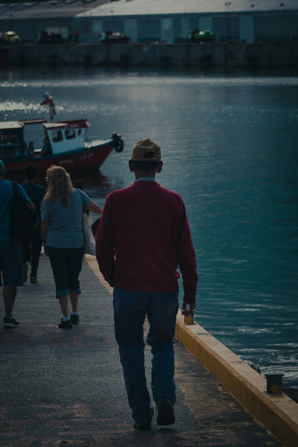 man in red hoodie standing beside woman in black pants on dock during daytime