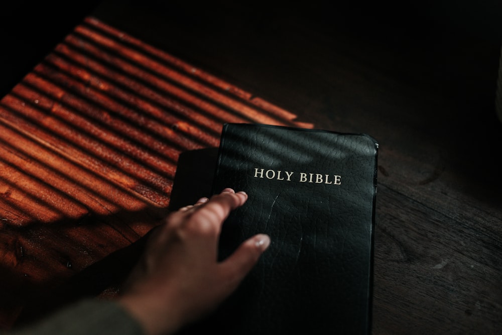 person holding black book on brown wooden surface