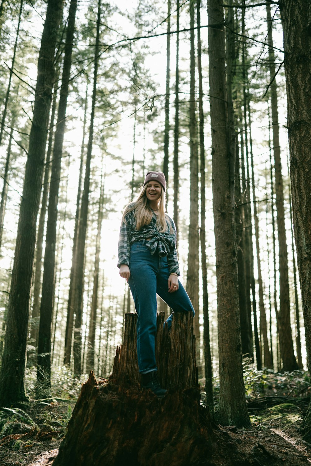 woman in gray long sleeve shirt and blue pants standing on brown tree trunk during daytime