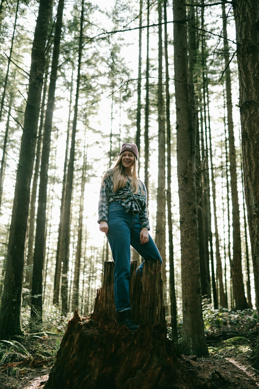 donna in camicia grigia a maniche lunghe e pantaloni blu in piedi sul tronco d'albero marrone durante il giorno