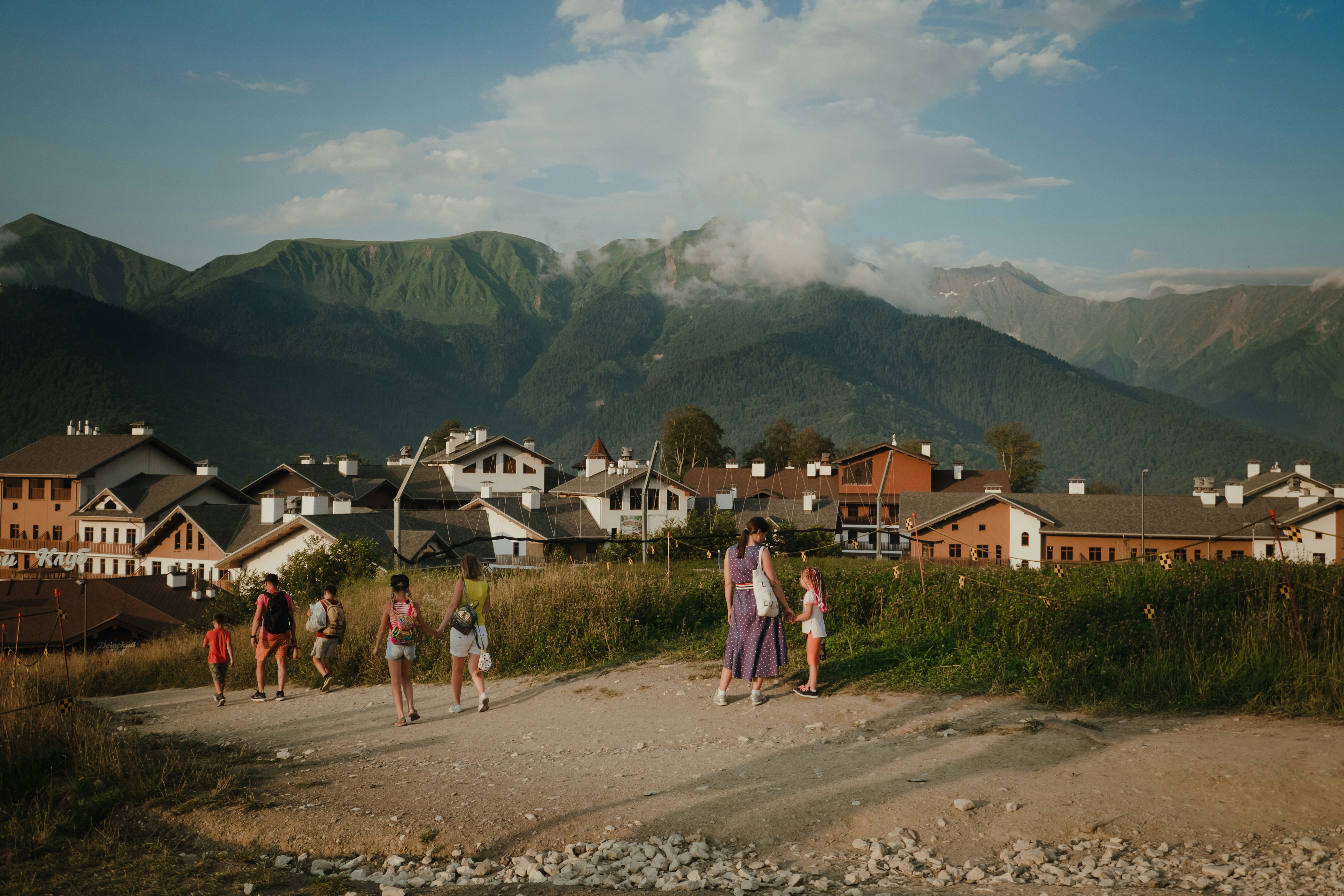 people walking on dirt road near houses and mountains during daytime