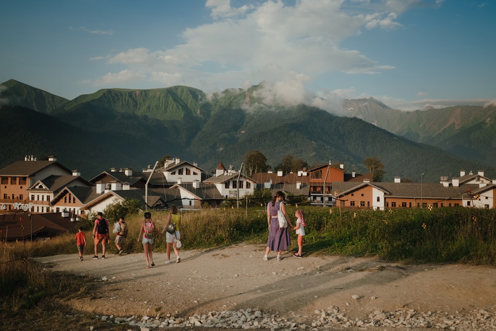 personas que caminan por caminos de tierra cerca de casas y montañas durante el día
