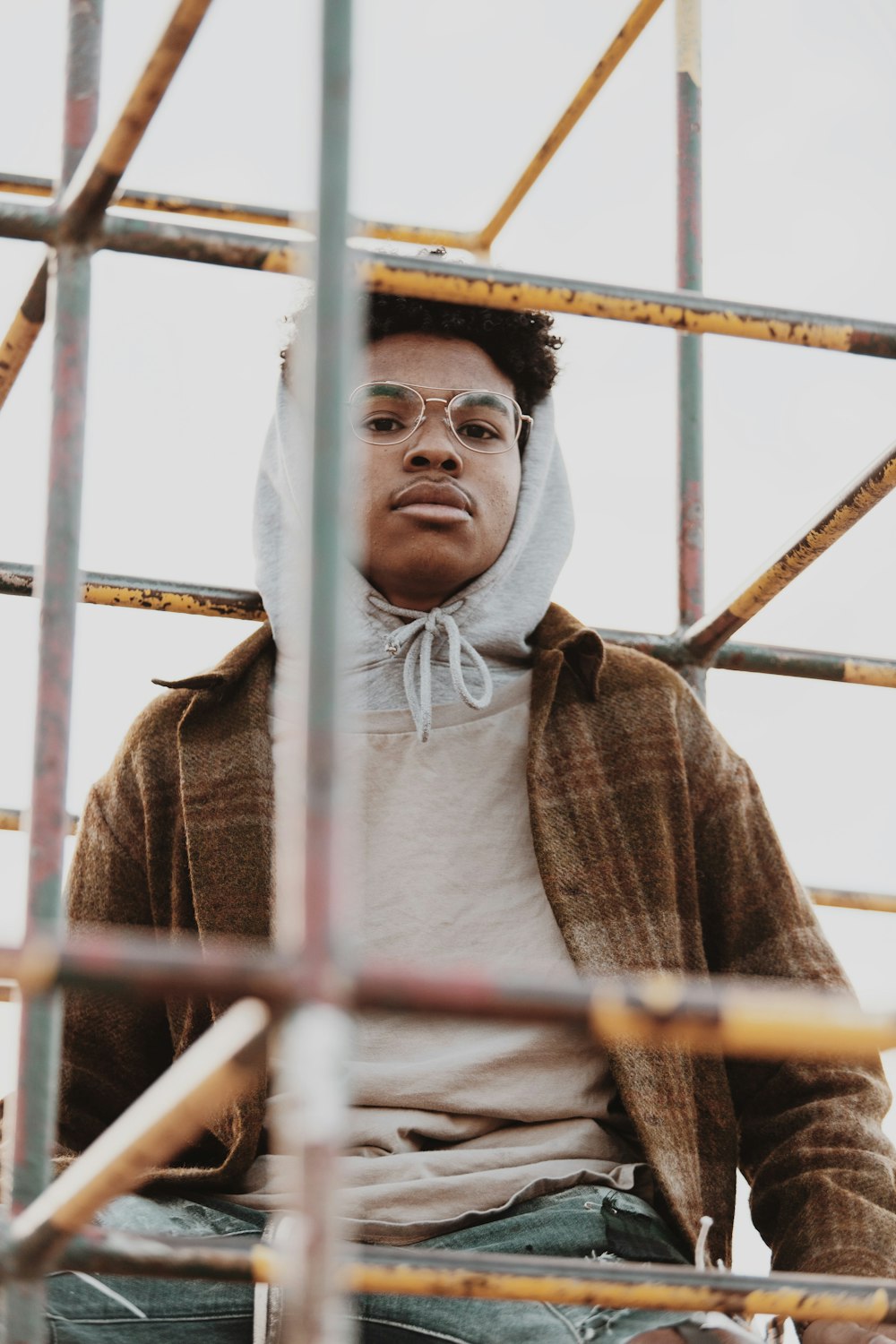 man in gray hoodie standing beside yellow metal fence