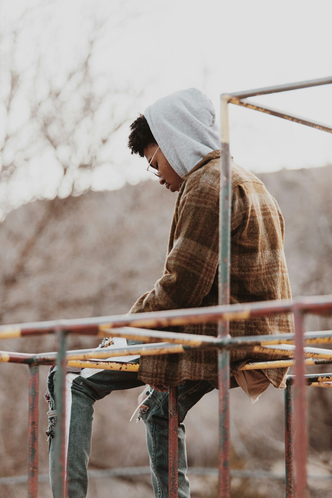 man in brown and black plaid dress shirt sitting on brown wooden fence during daytime