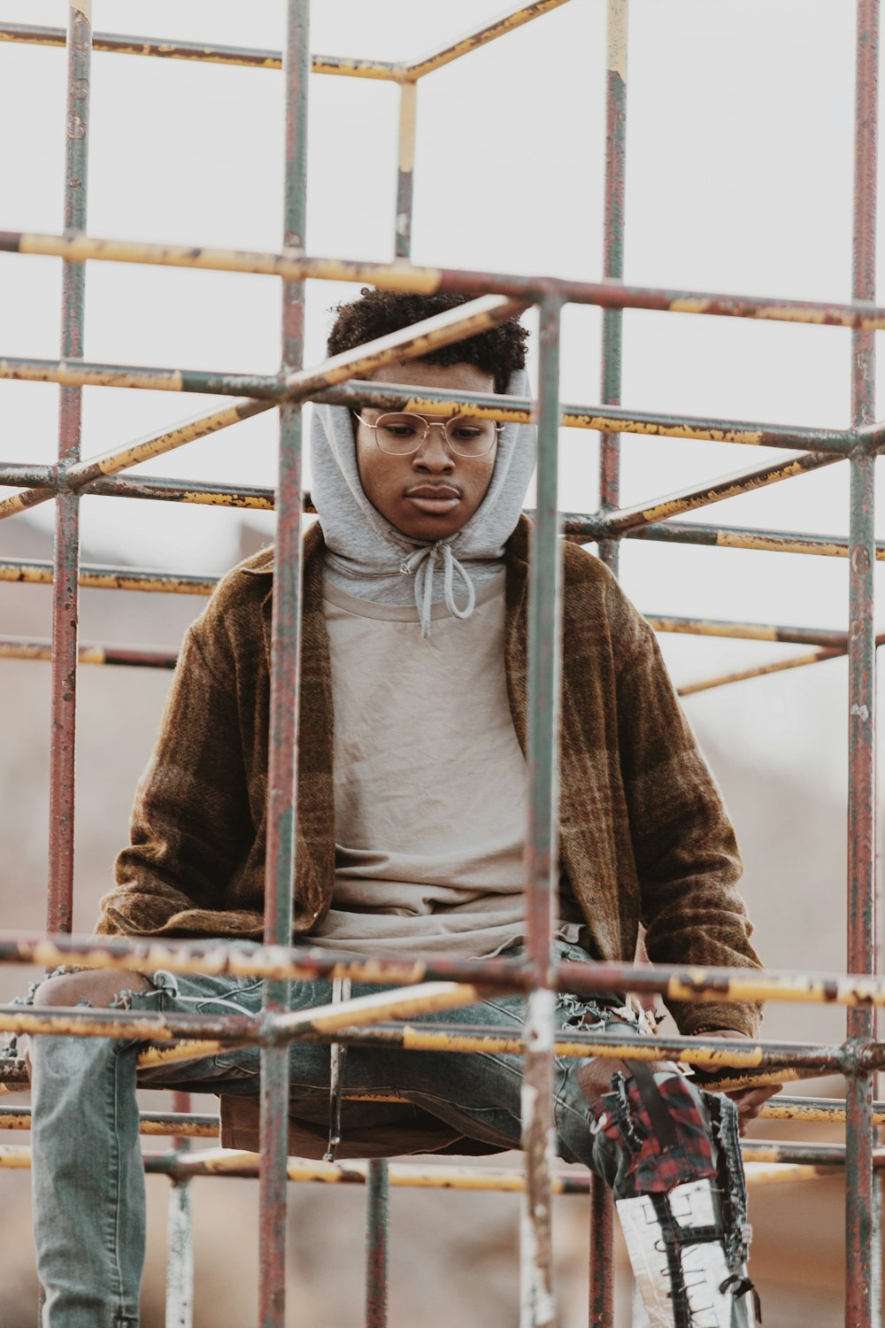 man in brown and gray sweater standing beside yellow metal fence