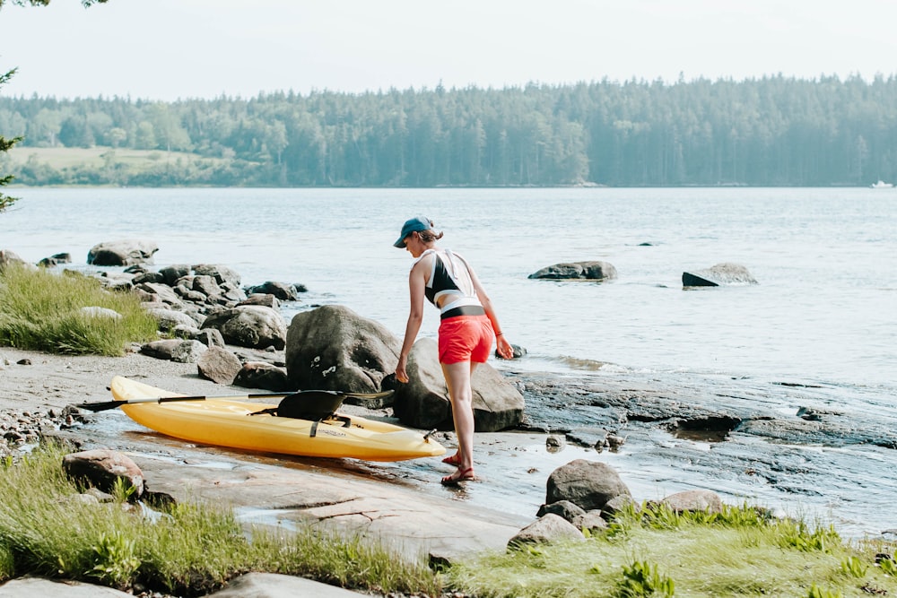 man in blue tank top and black shorts holding yellow surfboard on body of water during