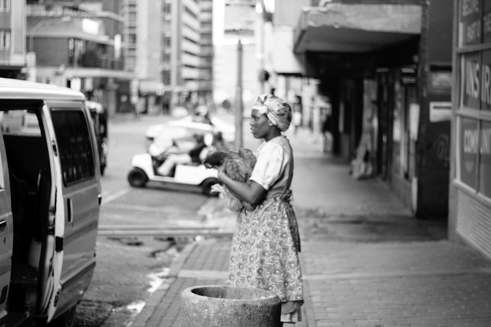 grayscale photo of woman in dress standing on sidewalk