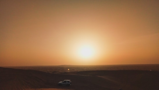 A stunning sunset over golden sand dunes with a silhouette of a 4x4 vehicle in motion.