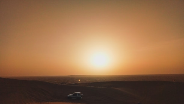 A vibrant sunset over rolling golden sand dunes with a 4x4 vehicle kicking up dust.