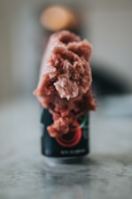 A can with a frozen pink slush overflowing from the top. The focus is on the ice formation, which appears textured and frosty. The background is blurred, suggesting a shallow depth of field.