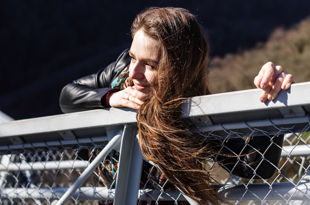 woman in black leather jacket leaning on gray metal railings during daytime