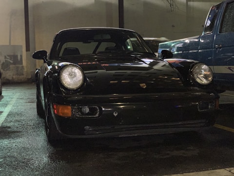A sleek black Porsche being carefully unloaded from a luxury transport truck at a modern garage.
