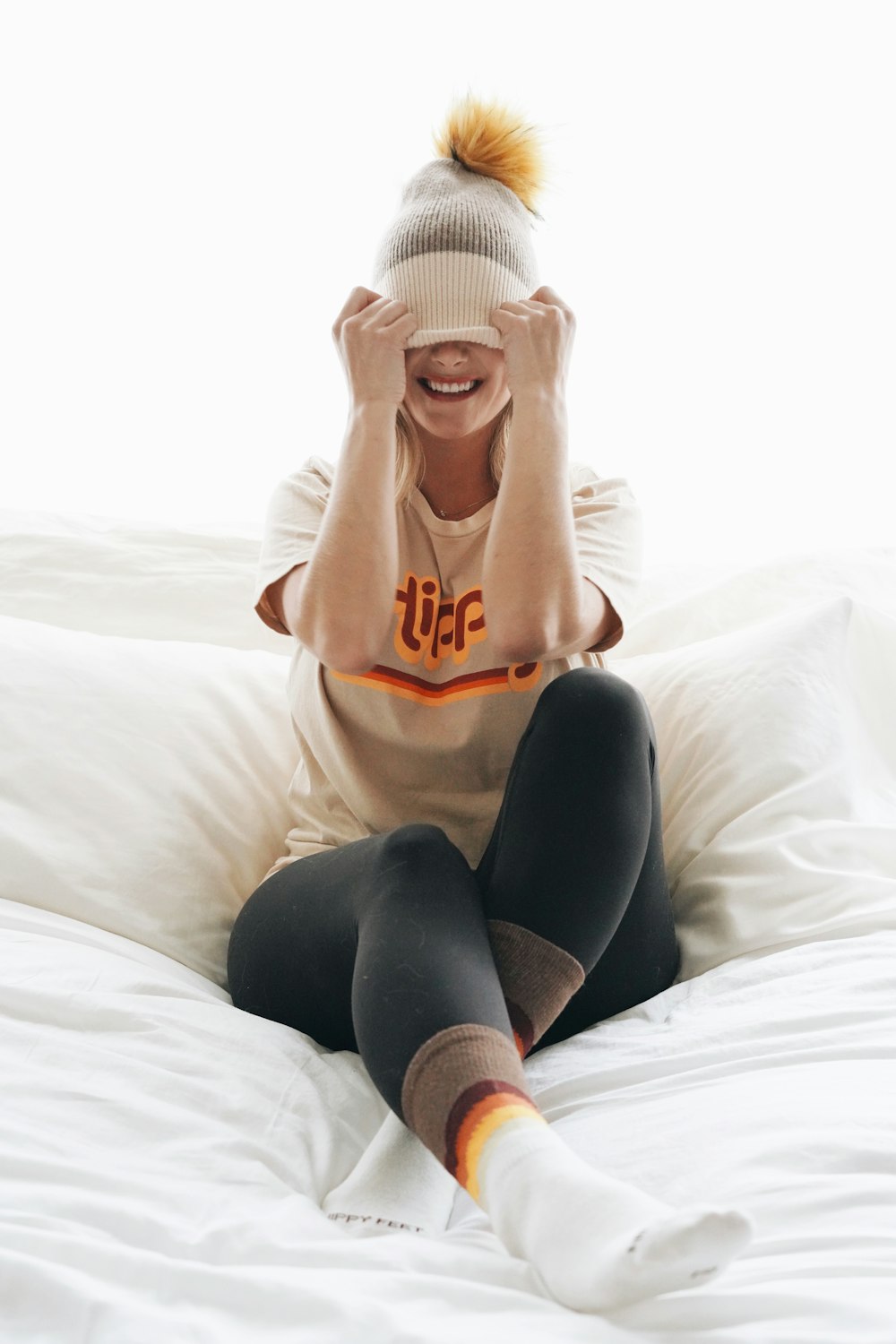 woman in white and red crew neck t-shirt and black shorts sitting on white bed