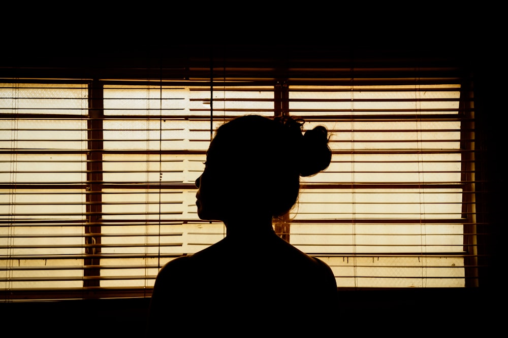窓のブラインドの近くに立っている女性のシルエット
