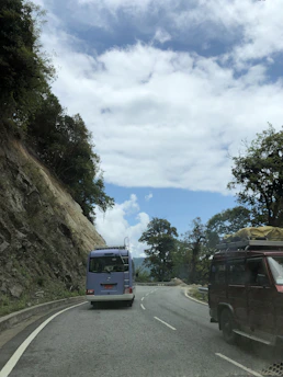 A sleek navy blue bus winding through Arunachal Pradesh's lush green mountains under a clear sky.