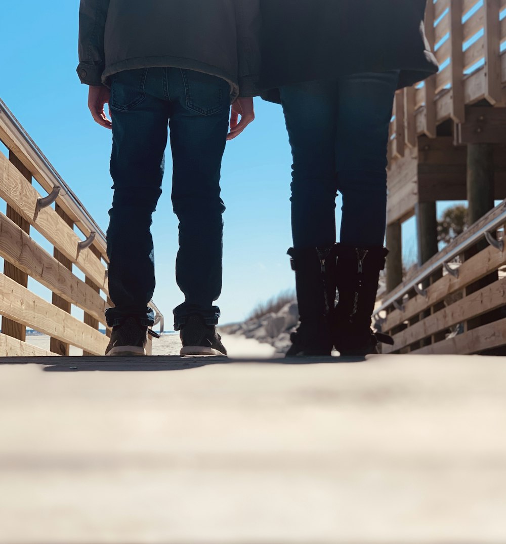 person in blue denim jeans and black boots standing on brown wooden stairs during daytime