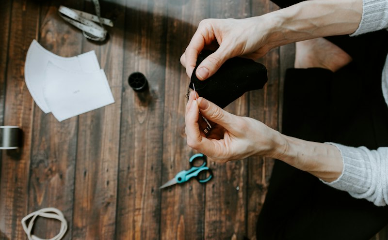 Les mains d’une artisane qui découpe un tissu noir, des ciseaux à côté