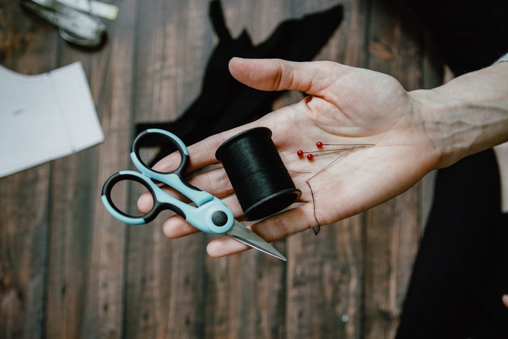 person holding black thread spool and silver scissors