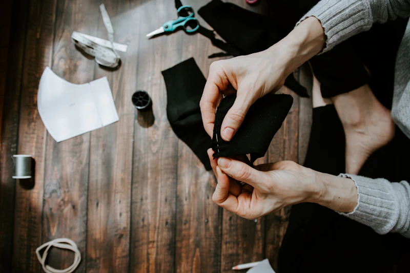 A pair of hands mending dark fabric, with scissors and thread nearby