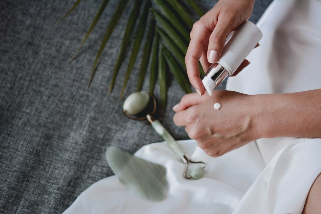 person holding white plastic bottle pouring white liquid on white ceramic mug, Facial massage with gua sha and jade roll