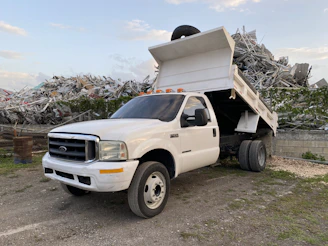 A flatbed truck arriving to pick up a scrap vehicle from a residential driveway.