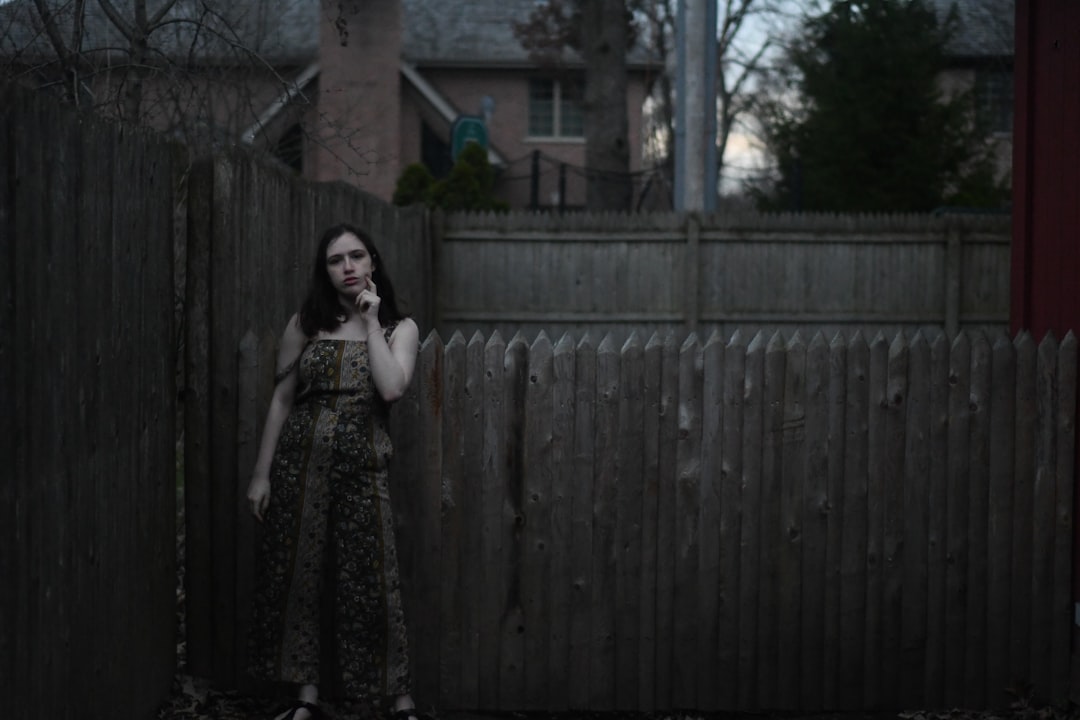 woman in black and brown floral dress standing beside brown wooden fence