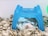 A small, white and brown hamster is resting inside a blue plastic house on a bed of shredded paper bedding. The hamster appears to be relaxed and cozy within its habitat.
