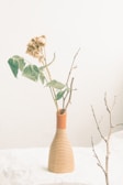A minimalist still life of a ceramic vase with dried wildflowers against a soft beige background.