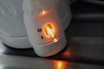 A close-up of a white appliance with a glowing orange indicator light next to a switch marked with 'I' and 'O'. The appliance is situated on a metallic surface.