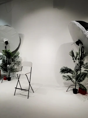 A white photo studio with two softbox lights and a folding chair