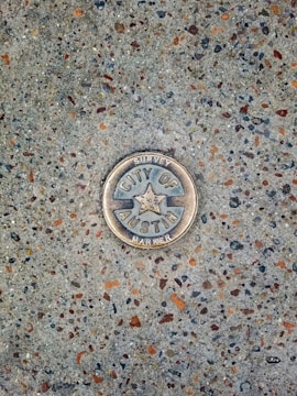 A metal survey marker is embedded in a textured concrete surface. The marker features a star in the center and has the words 'City of Austin Survey Marker' engraved on it. The concrete is speckled with various shades of gray, brown, and orange.