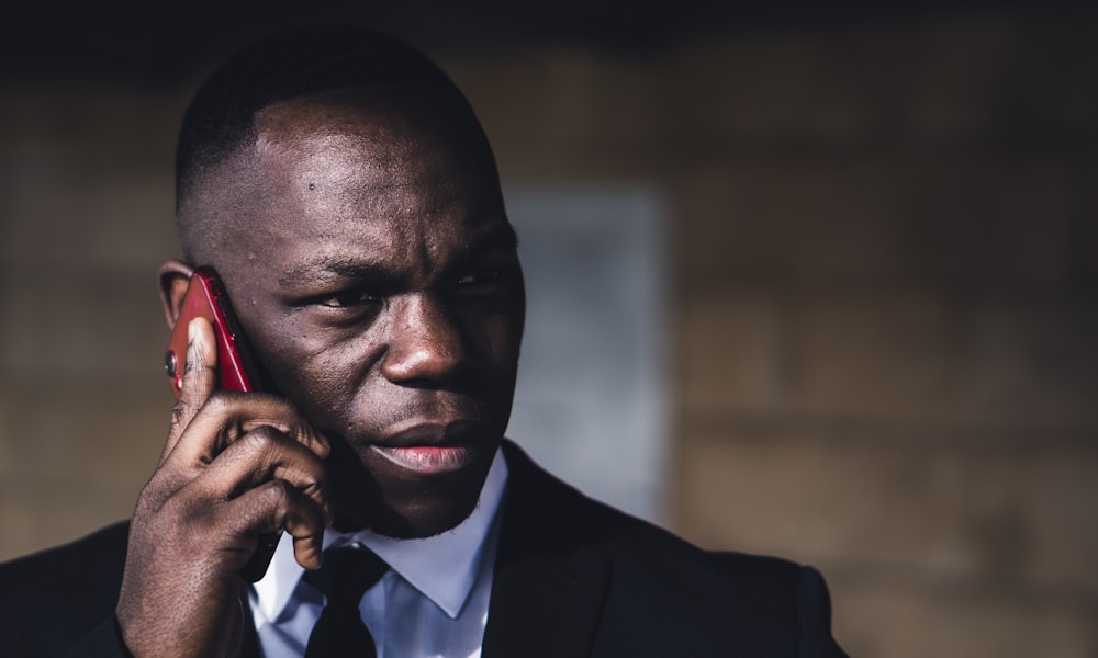 man in black suit holding red smartphone