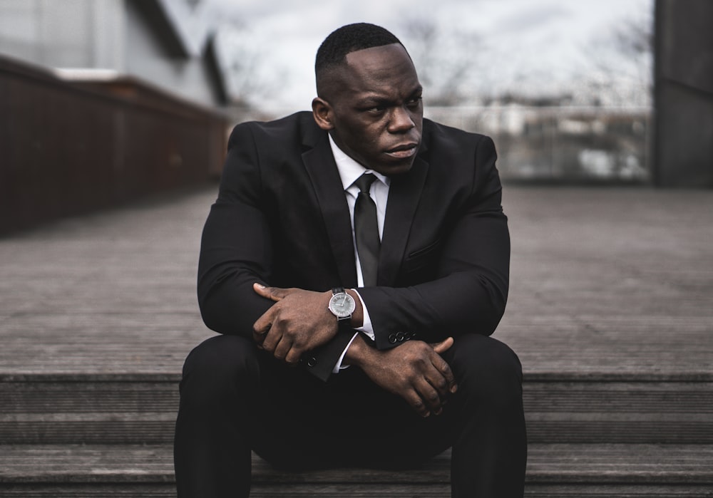 man in black suit sitting on brown wooden bench