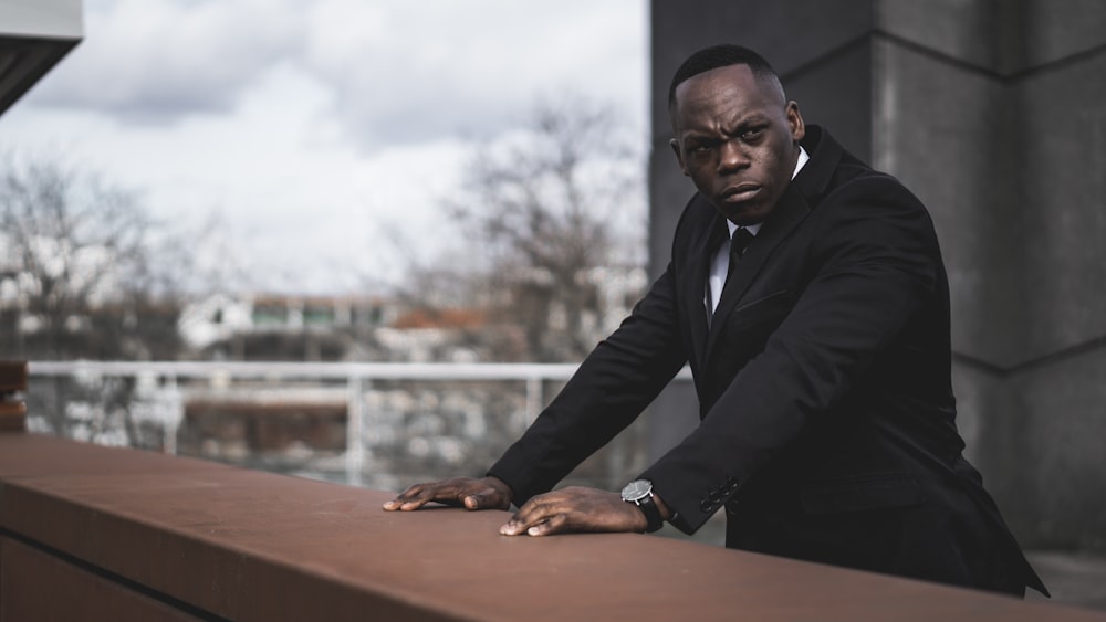 man in black suit jacket sitting on brown wooden bench during daytime