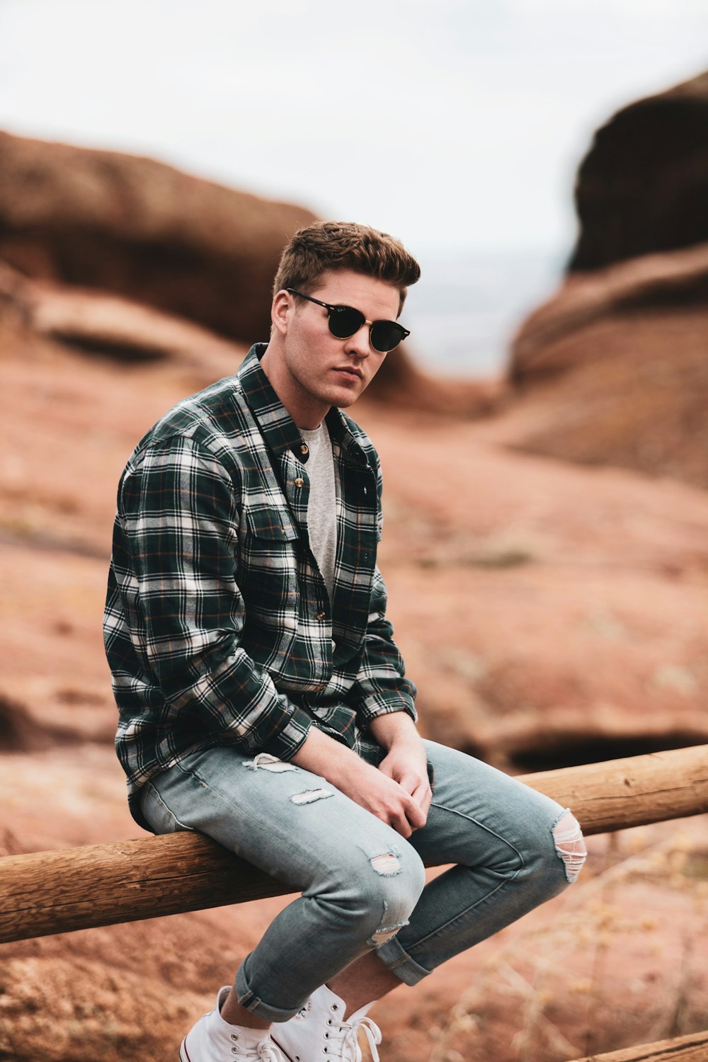 man in blue white and black plaid dress shirt and gray denim jeans sitting on brown