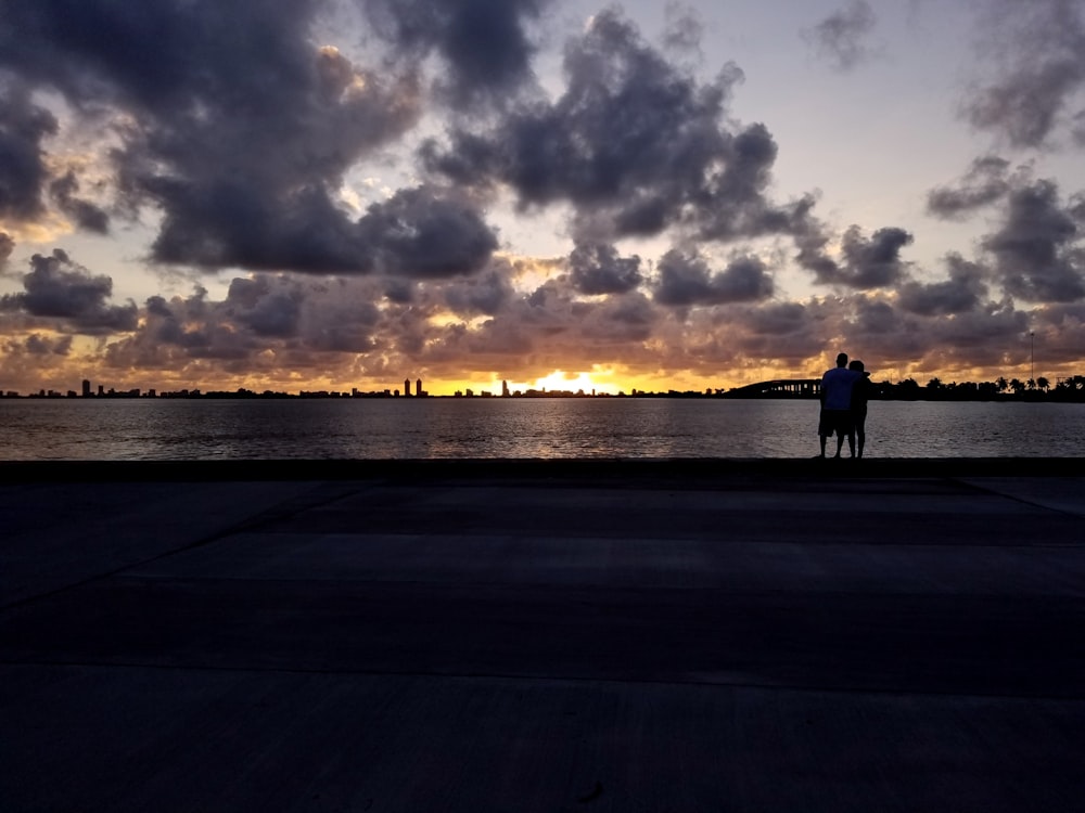 silhueta de 2 pessoas em pé à beira-mar durante o pôr do sol