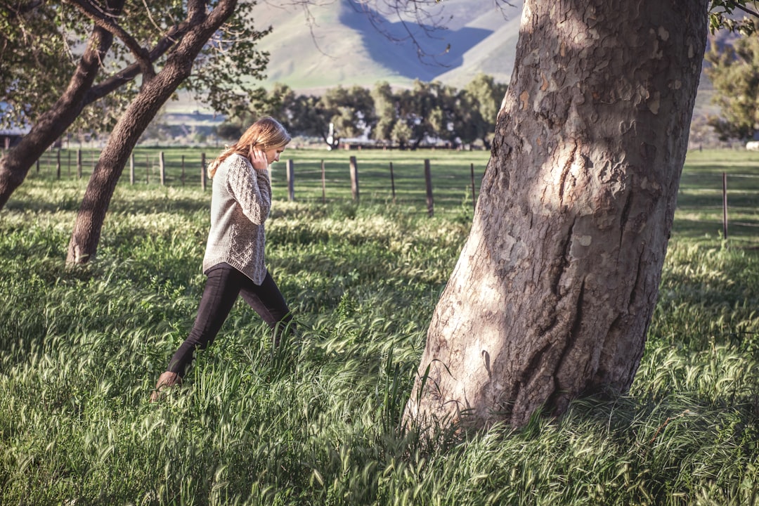 woman in white and black long sleeve shirt standing beside brown tree during daytime