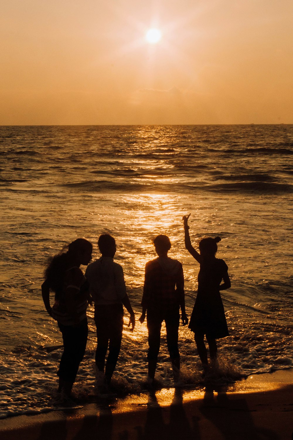 silhouette of people standing on seashore during sunset