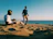 A person listening to an audiobook with headphones, sitting on a sunny beach.