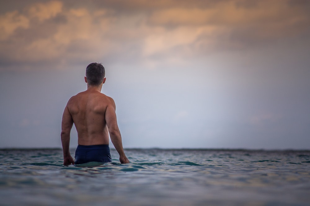 topless man in blue shorts standing on water during daytime