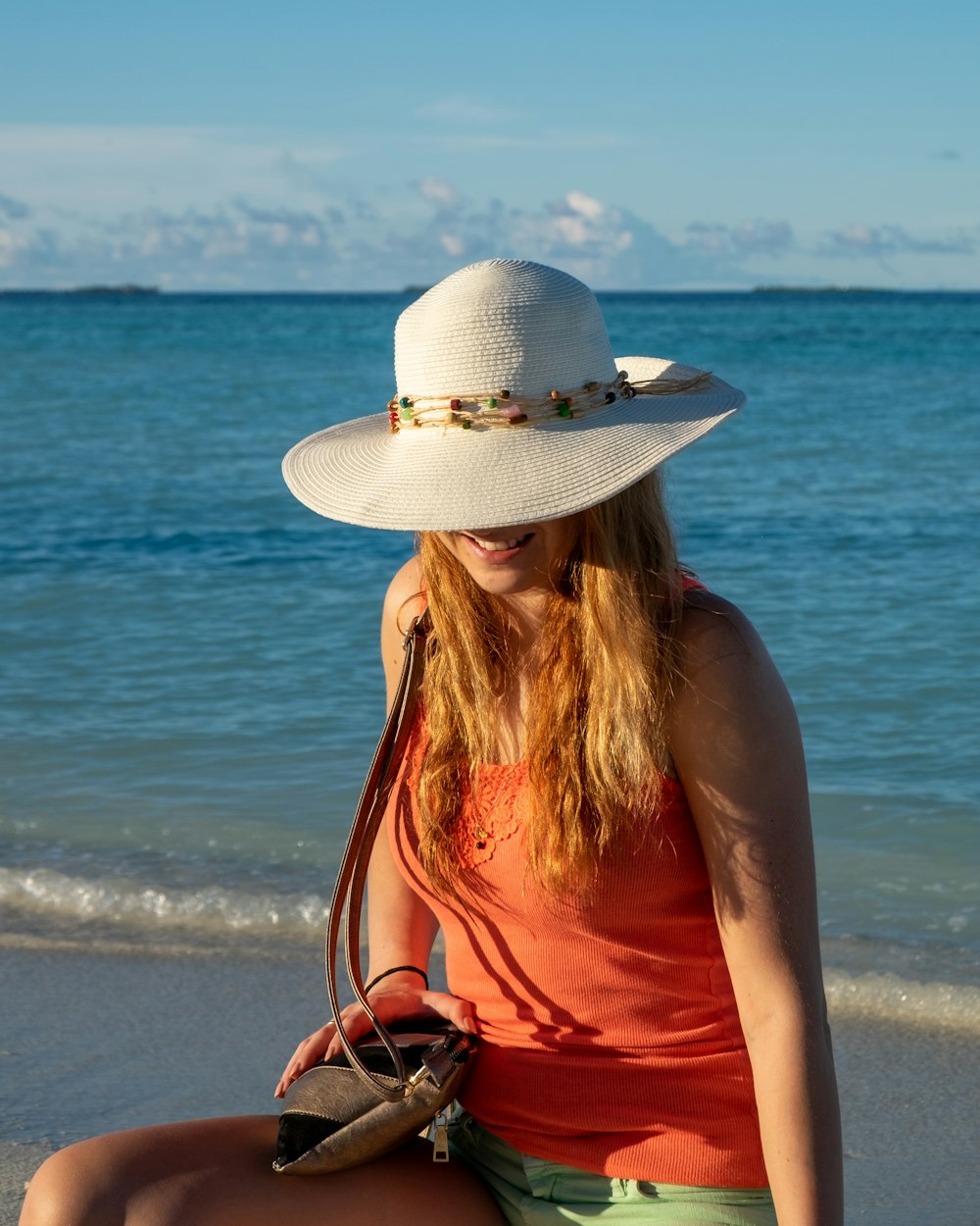 woman in red tank top wearing white sun hat standing on beach during daytime