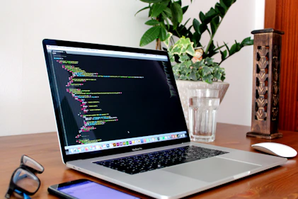 A sleek laptop open on a minimalist desk with coding on the screen.