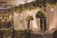 An elegantly decorated banquet setting featuring tall arrangements of white and cream flowers on stands, with cascading flowers overhead. Warm lighting from hanging bulbs adds a soft glow to the scene, complementing the flowing draped fabrics in the background and on the tables.