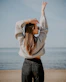 woman in white sweater and blue denim jeans standing on beach shore during daytime