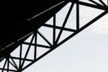 Geometric steel structure with intersecting beams against a light sky background.