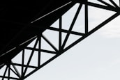 Geometric steel structure with intersecting beams against a light sky background.