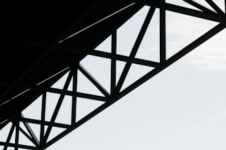 Geometric steel structure with intersecting beams against a light sky background.