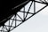 Geometric steel structure with intersecting beams against a light sky background.